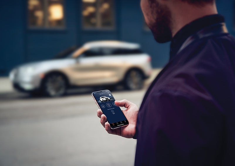 A person is shown interacting with a smartphone to connect to a Lincoln vehicle across the street. | Boulevard Lincoln in Georgetown DE